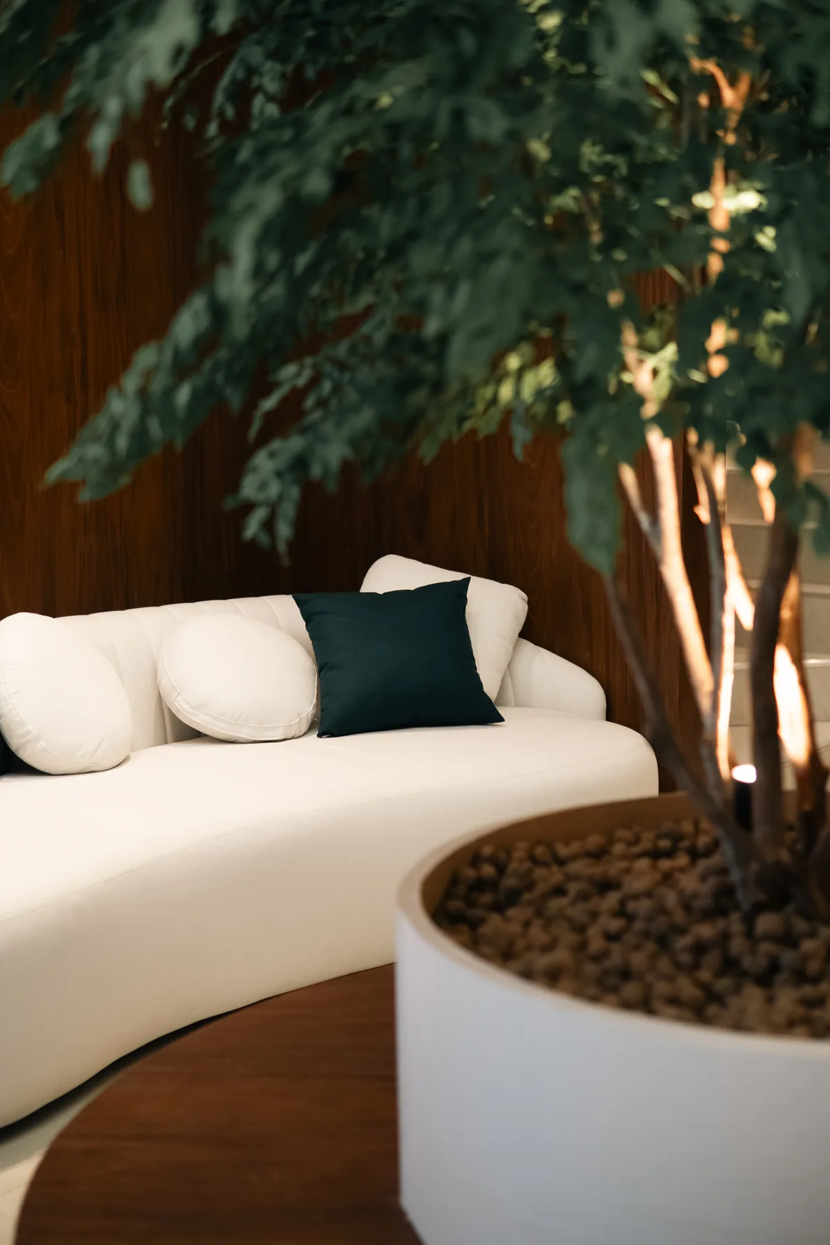 Sofá curvo branco na sala de espera com paisagismo interno e revestimento em madeira nobre